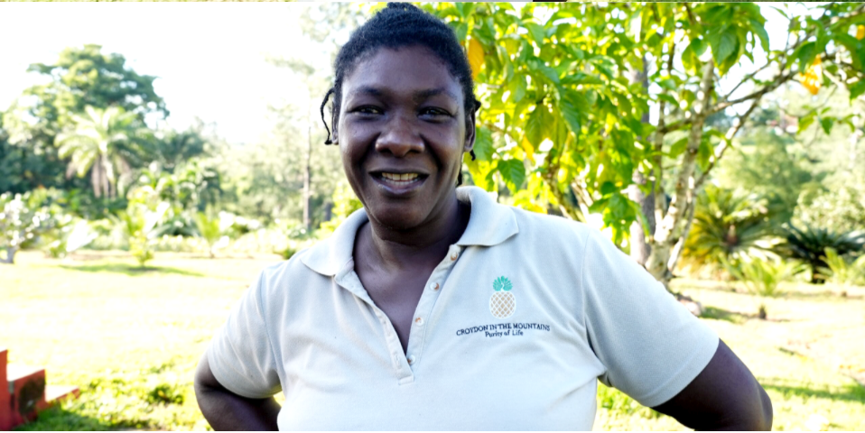 A woman in a white shirt is smiling in front of trees