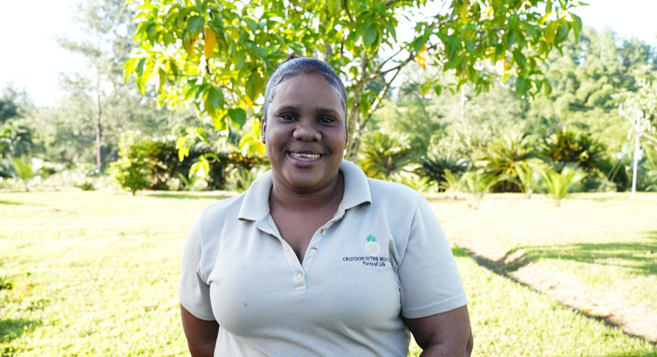 A woman in a white shirt is standing in front of a tree in a field.