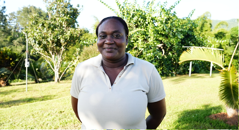 A woman in a white shirt is standing in a grassy field.