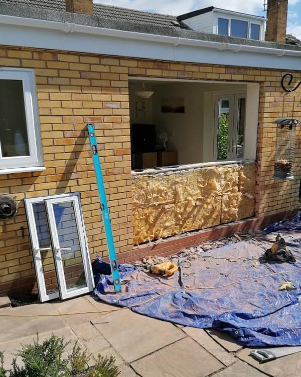 a brick building with a window being removed and a blue tarp on the ground .