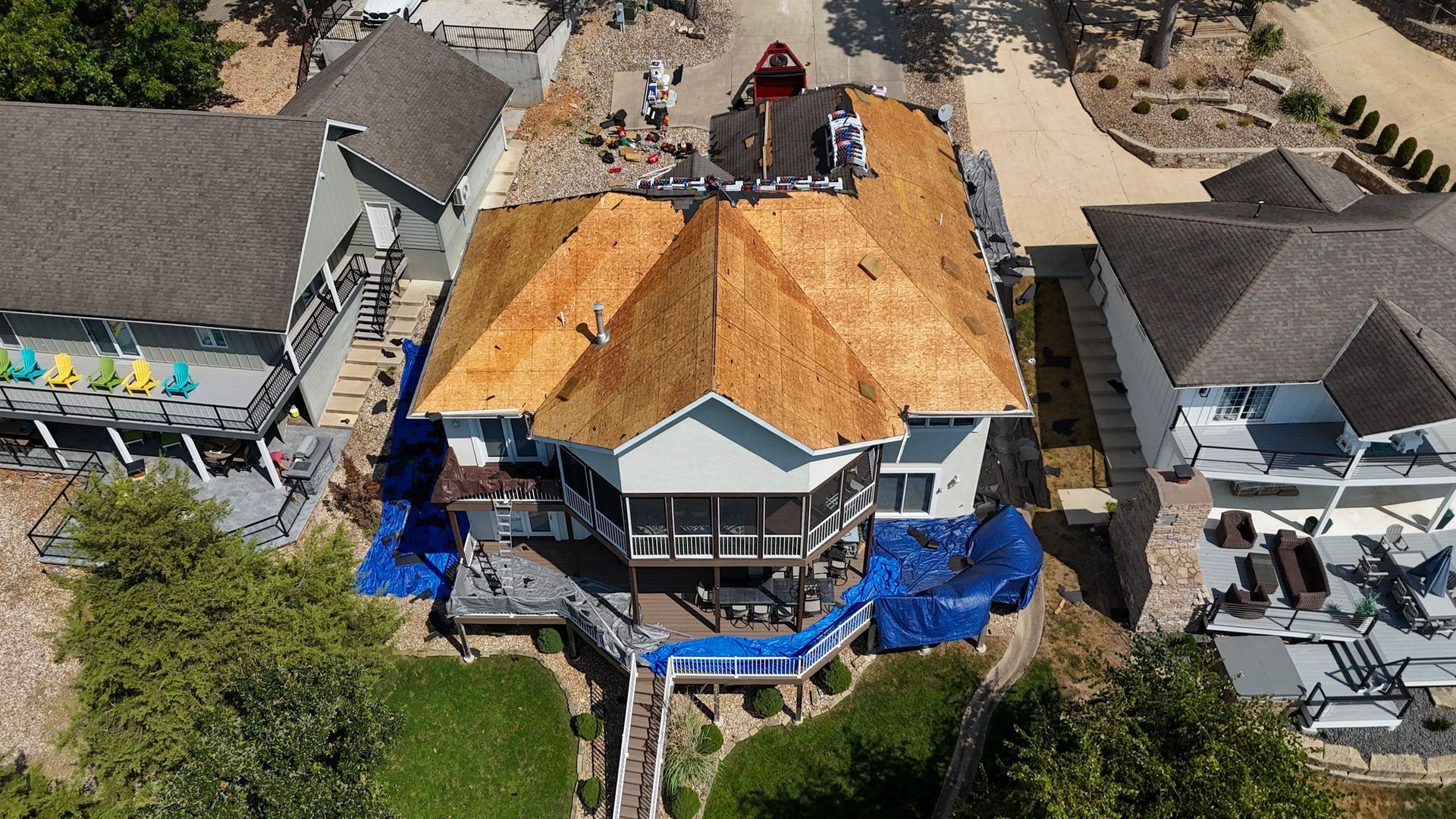 Aerial view of a house undergoing roof replacement, blue tarps cover the deck and surroundings.