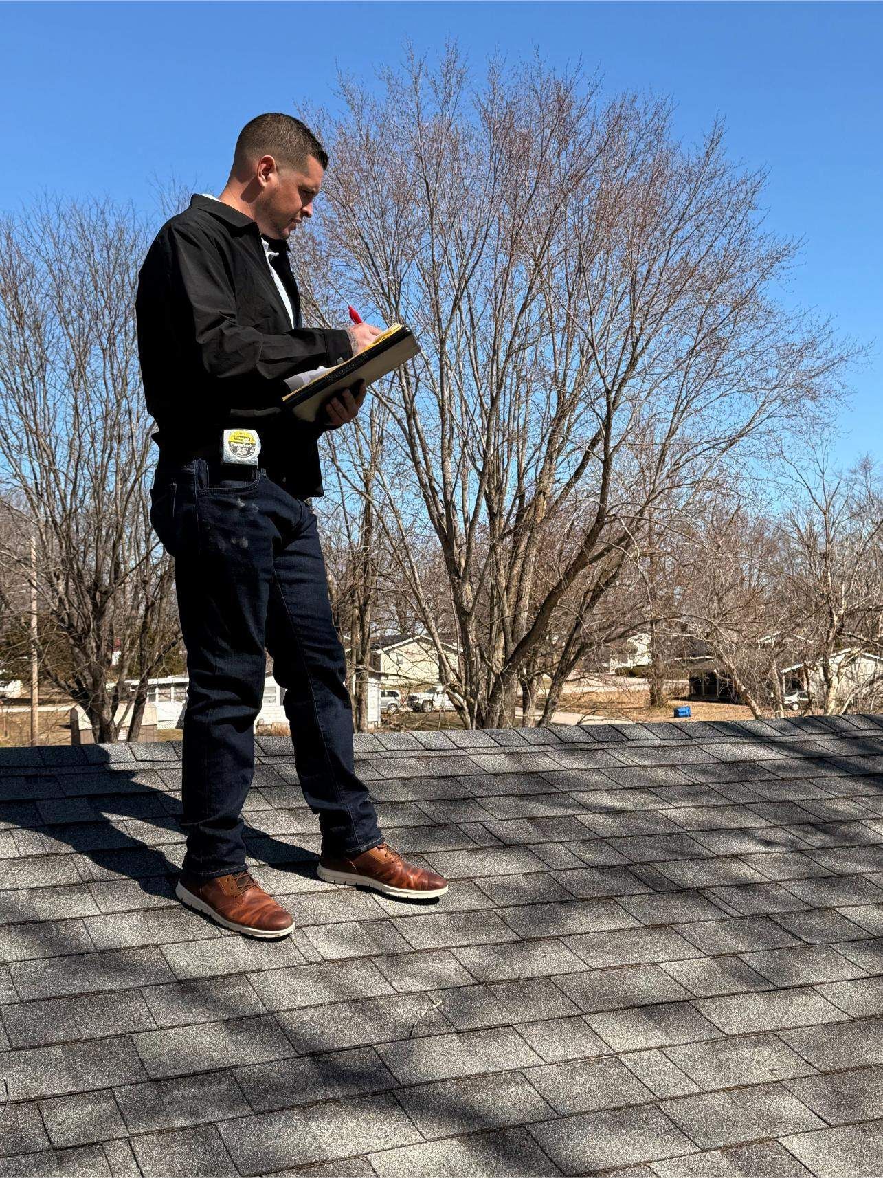 Person on a roof taking notes, inspecting shingles. Clear, sunny day.