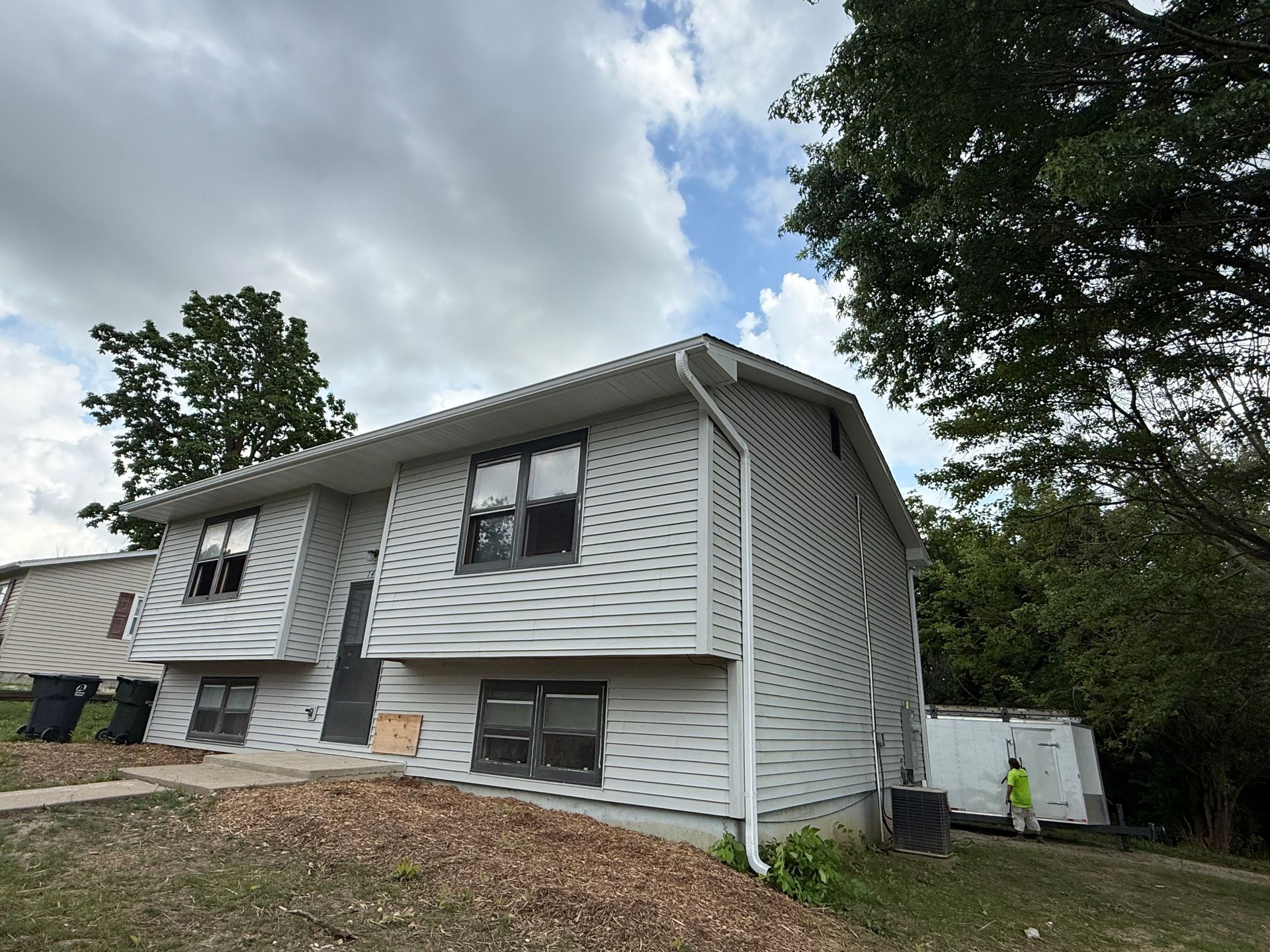 Two-story house with gray siding, white trim, gutters, and a cloudy sky.