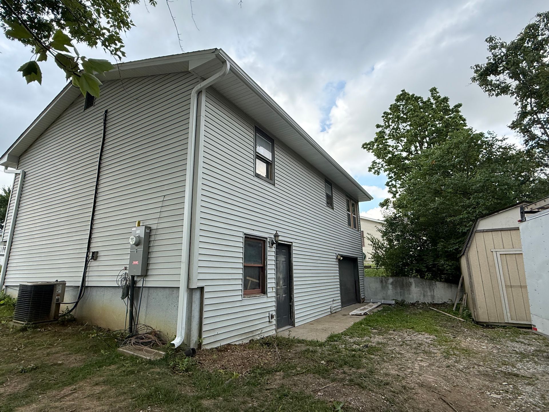 Two-story house with white siding, surrounded by grass and trees under a cloudy sky.
