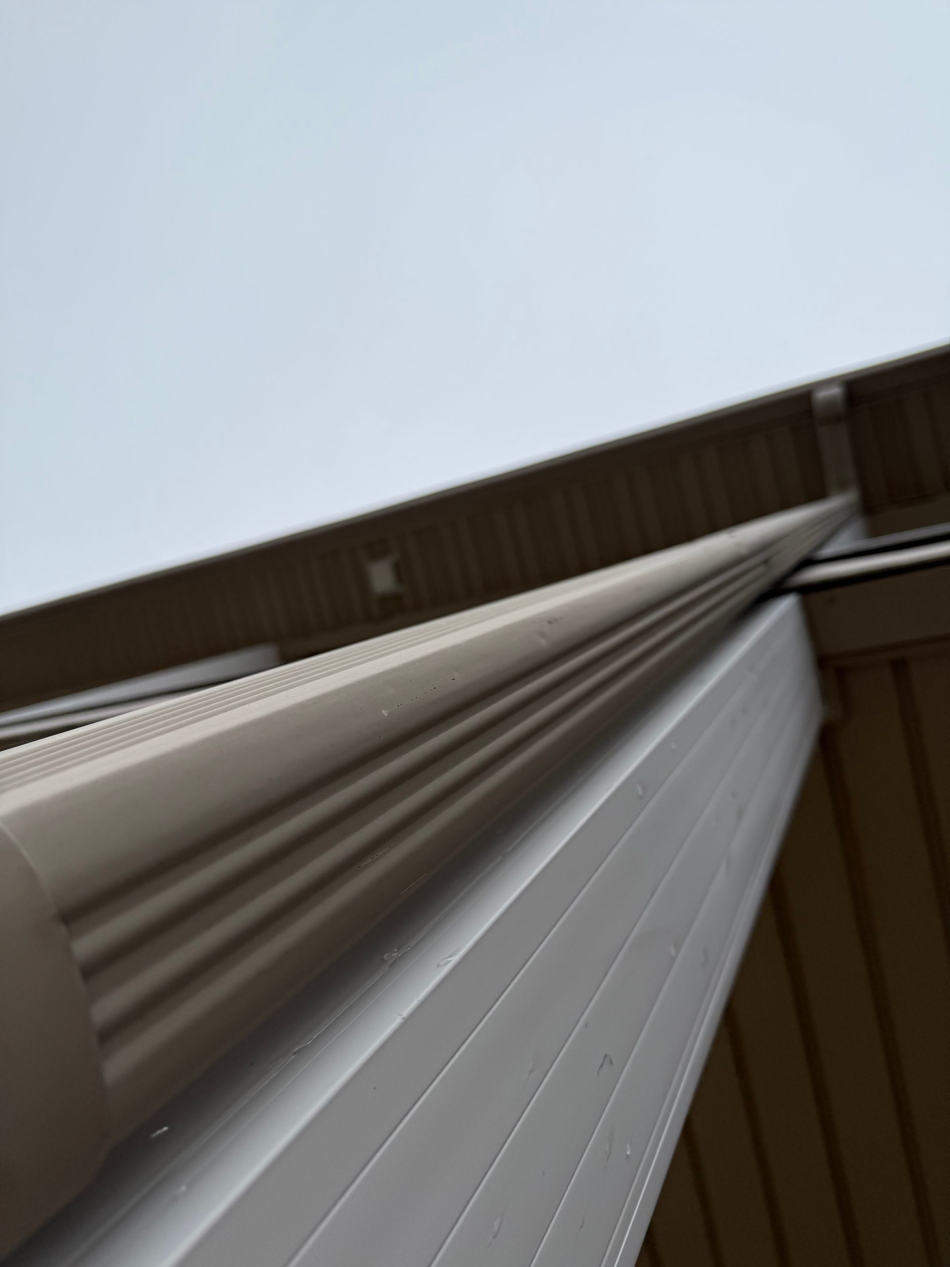 Construction site near water with insulation panels and machinery. Bare trees against blue sky.