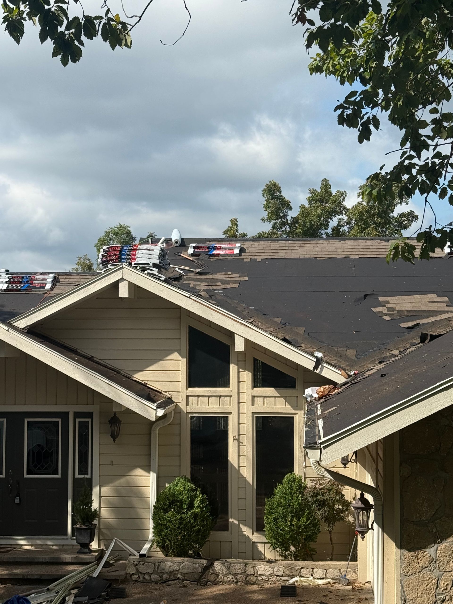 House with roof partially torn off; workers on roof; overcast sky.