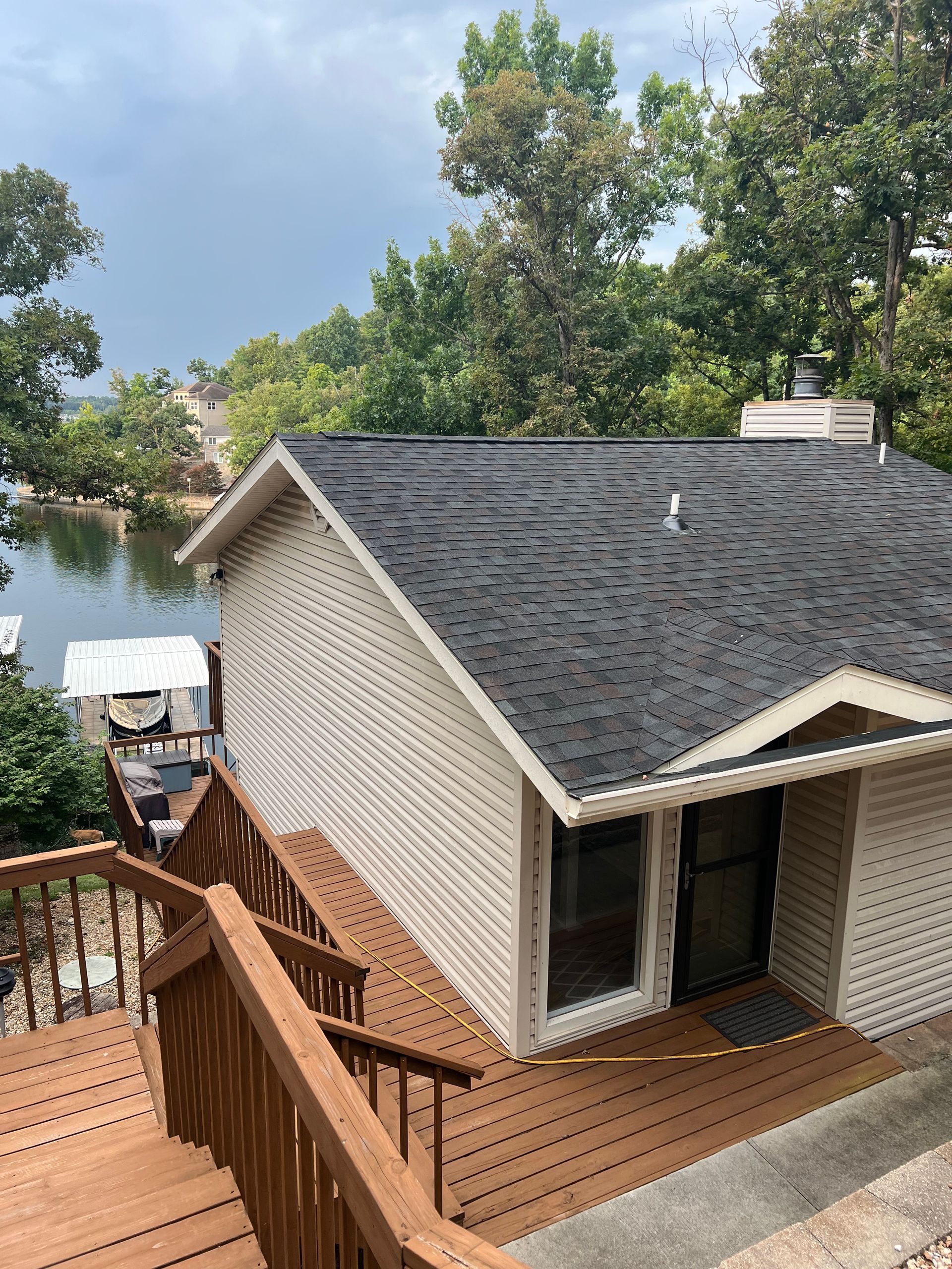 Workers on roof replacing shingles; white truck parked in front of two-story house, sunny day.