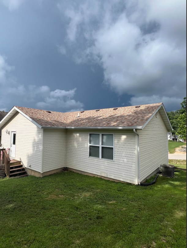 Beige house with brown roof and green lawn under a cloudy sky.