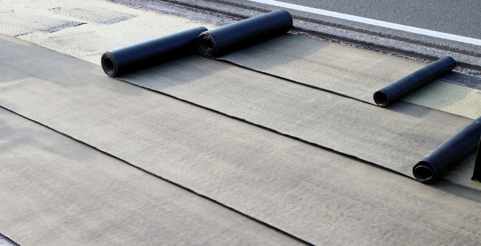 Black roofing material rolls on a gray, partially-installed roof.