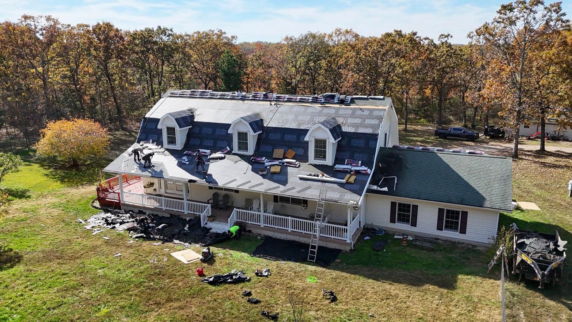 Damaged house after a fire with debris on the ground. Roof is partially destroyed; trees in background.
