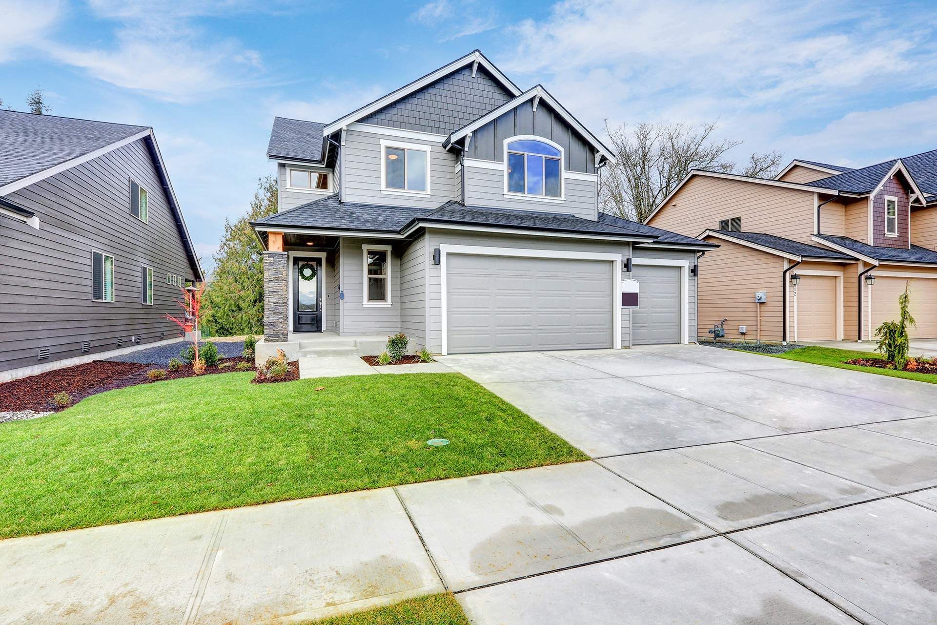 Gray two-story house with a two-car garage, green lawn, and concrete driveway on a sunny day.