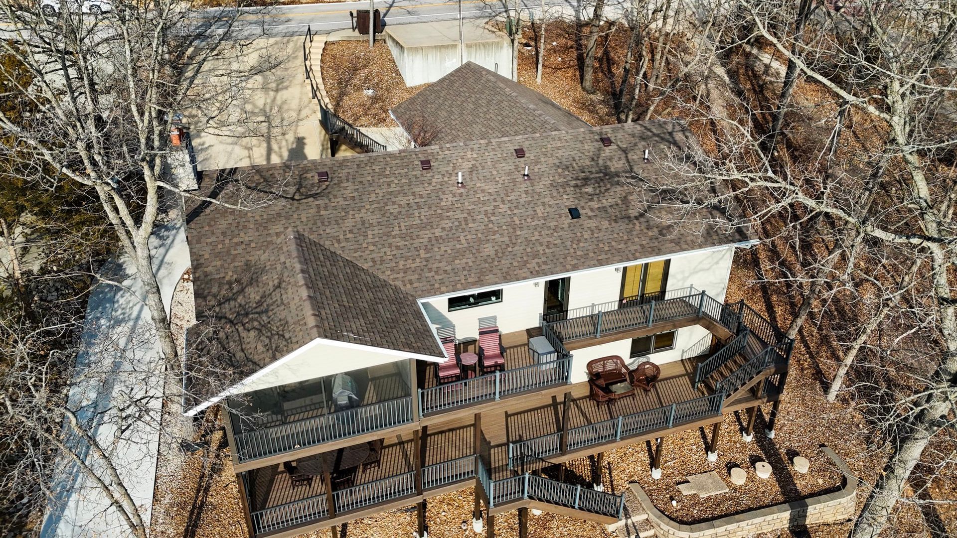 Aerial view of a house with a brown roof and a wooden deck overlooking a wooded area.