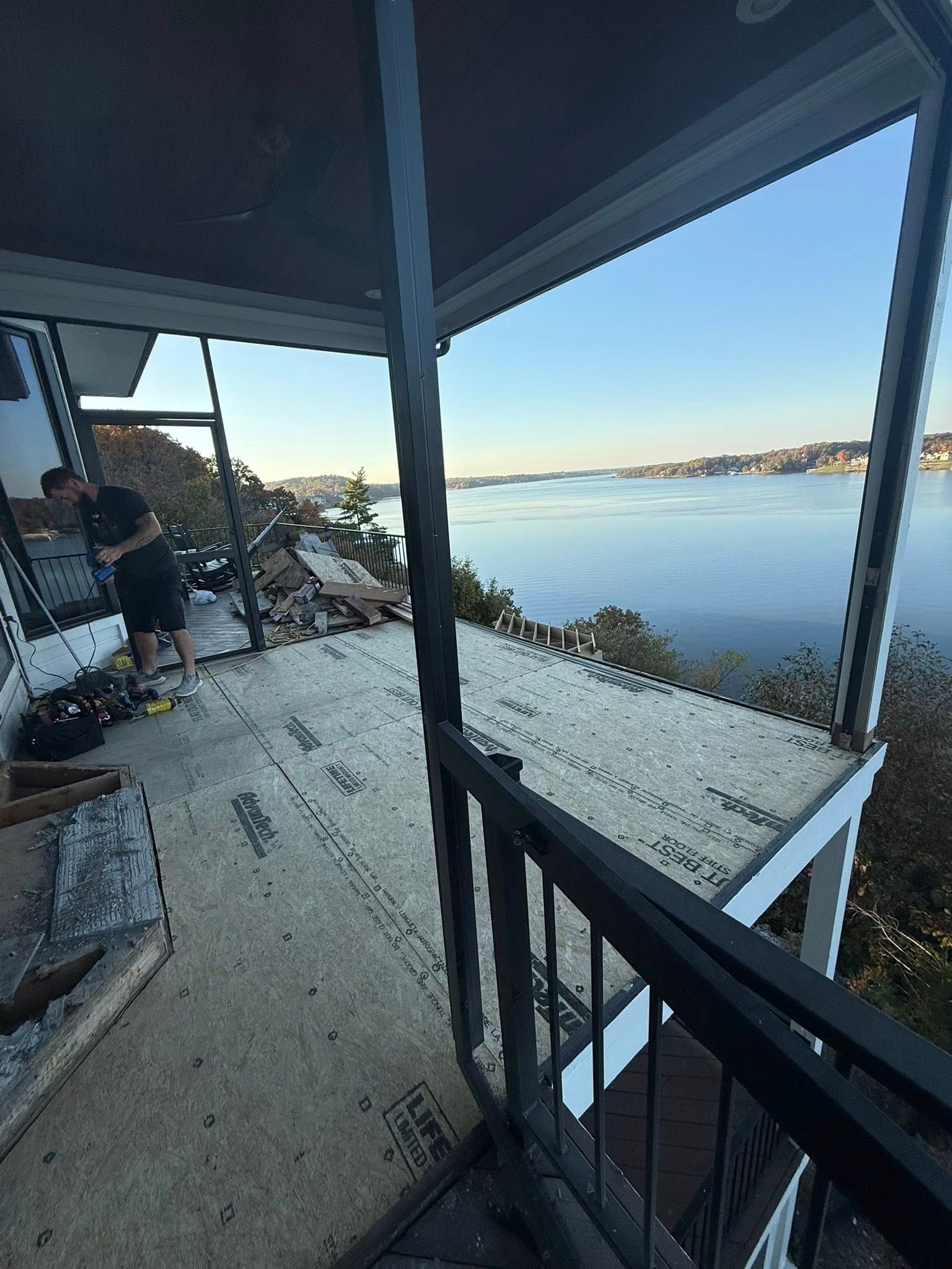 Person on deck overlooking a wide body of water and distant land. Blue sky above.