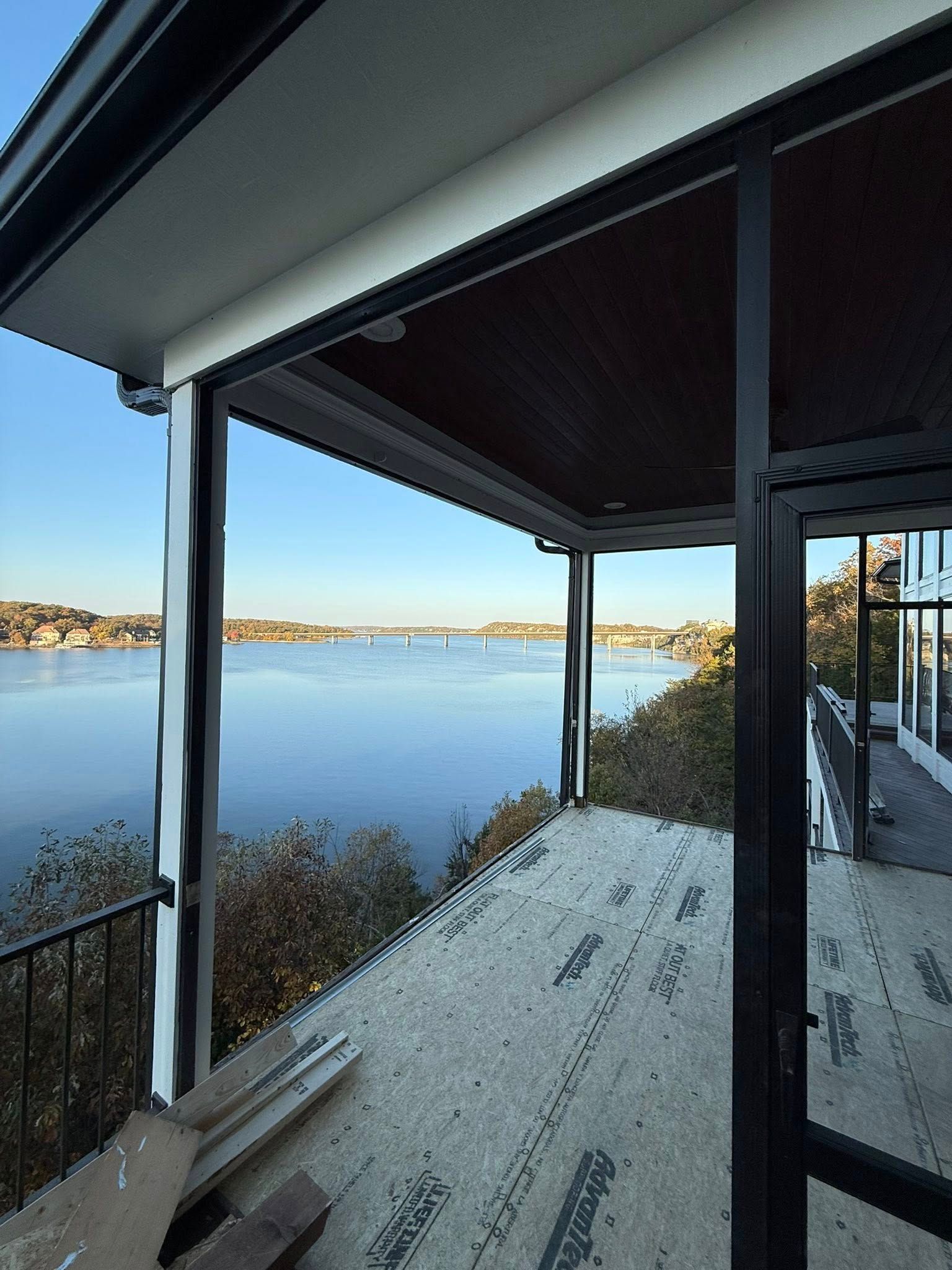 Open-air patio overlooking a wide body of water and bridge. The ceiling and framing are dark, with natural scenery in the distance.