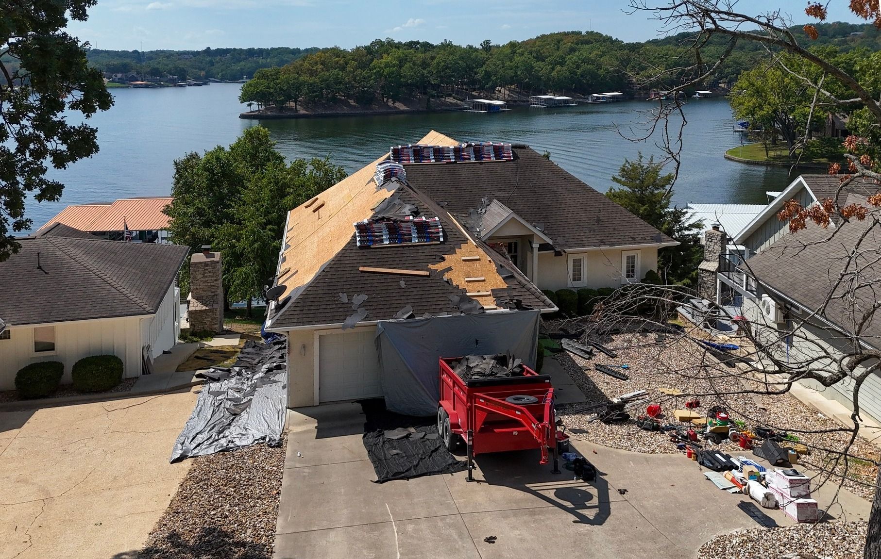 House roof replacement underway overlooking a lake; shingles and debris visible.