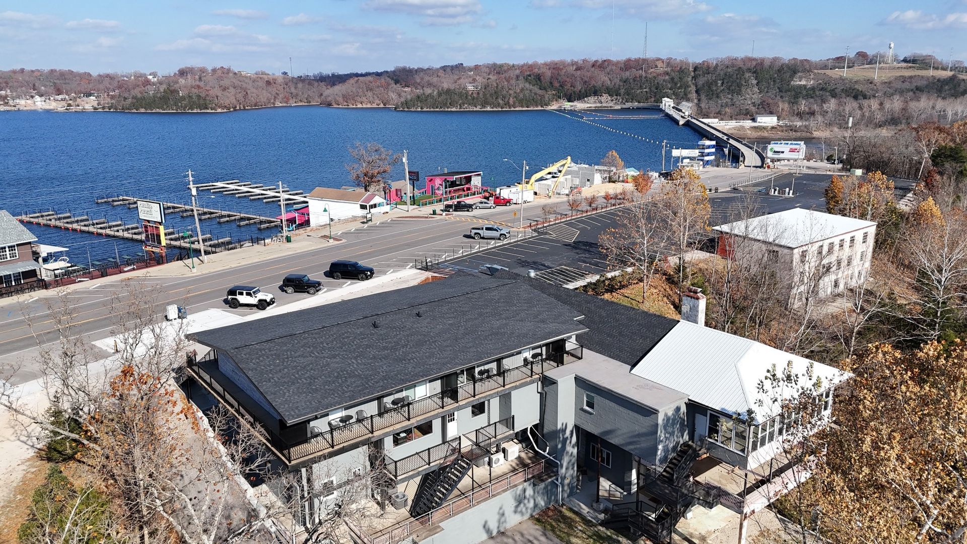 An aerial view of a lakeside town with buildings, a road with cars, and a bridge.