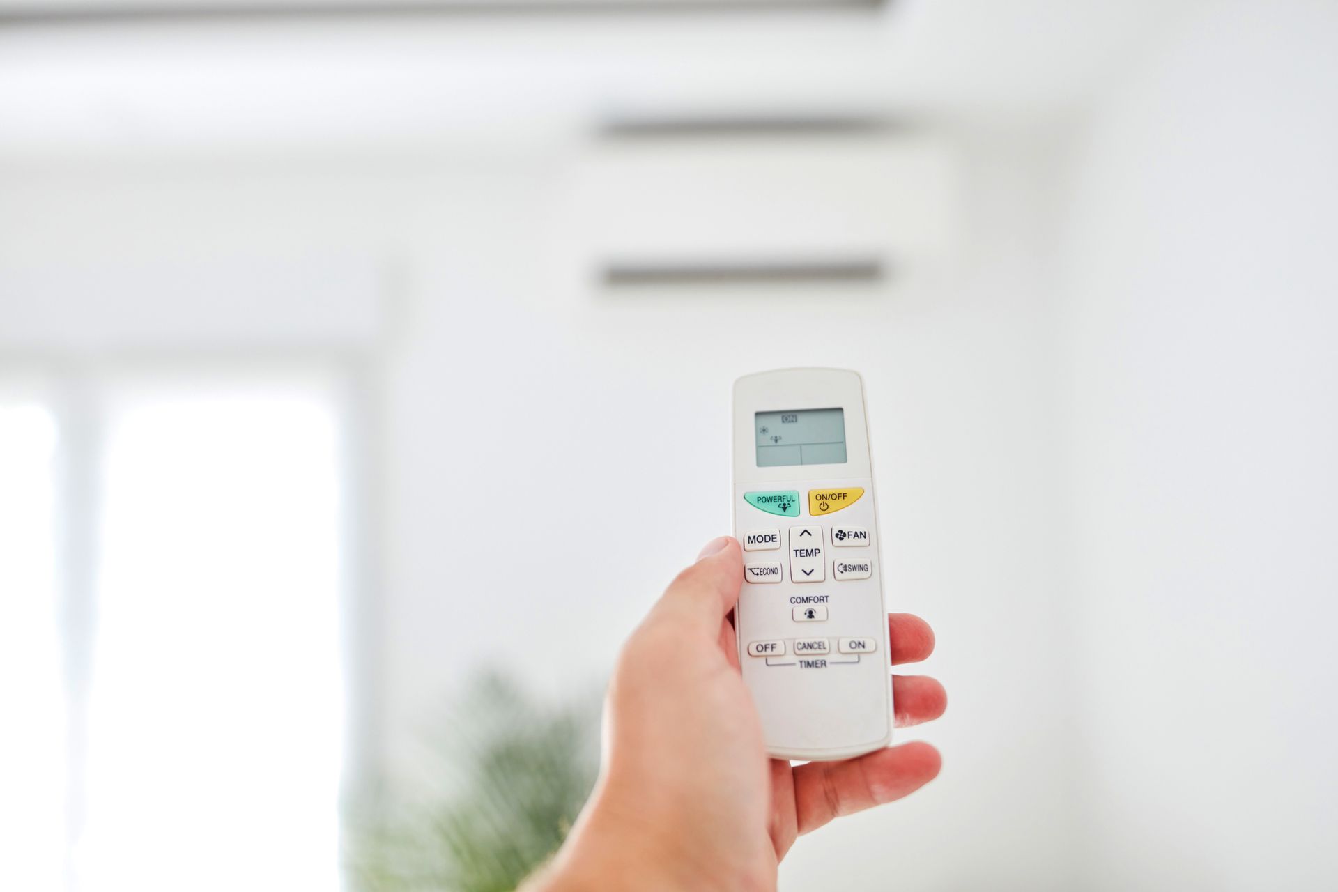 A person is holding a remote control in their hand in front of an air conditioner.