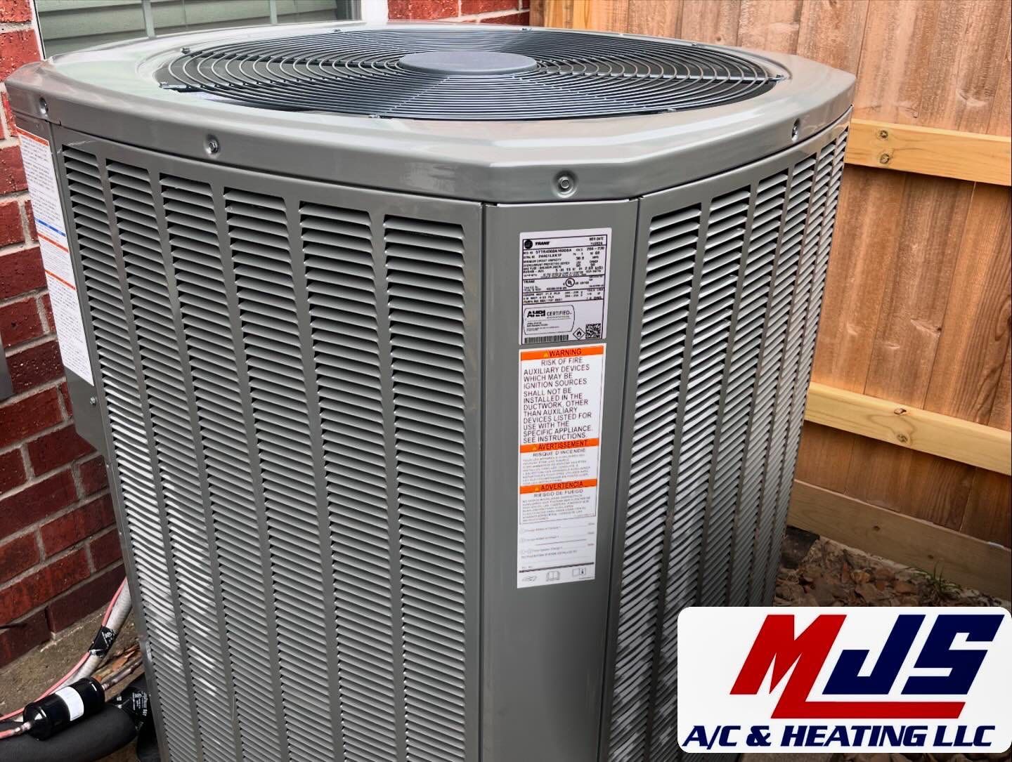 A gray air conditioning unit outside a building. MJS A/C & Heating LLC logo in the corner.