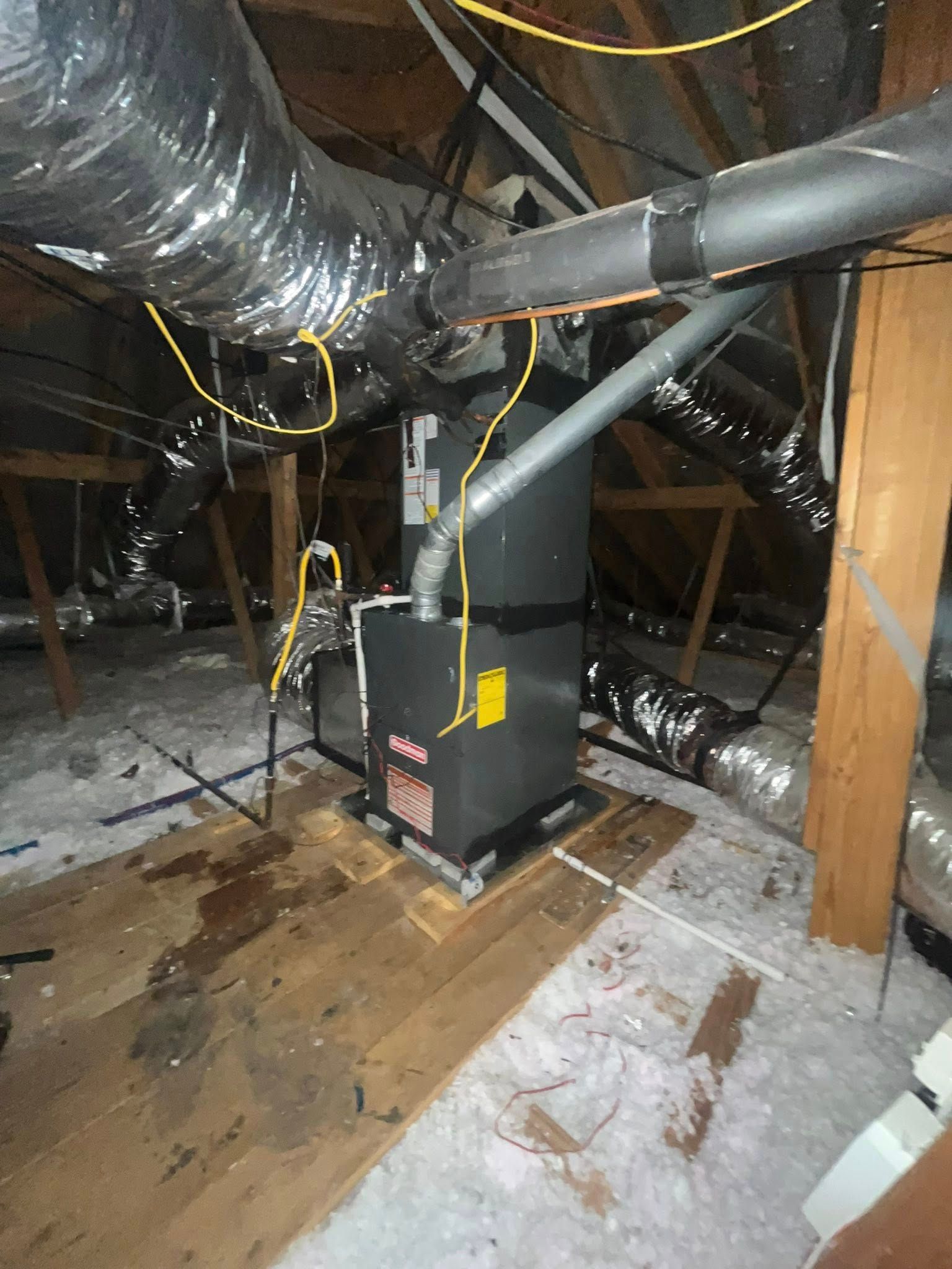 HVAC unit in an attic with ductwork, wooden supports, and insulation.