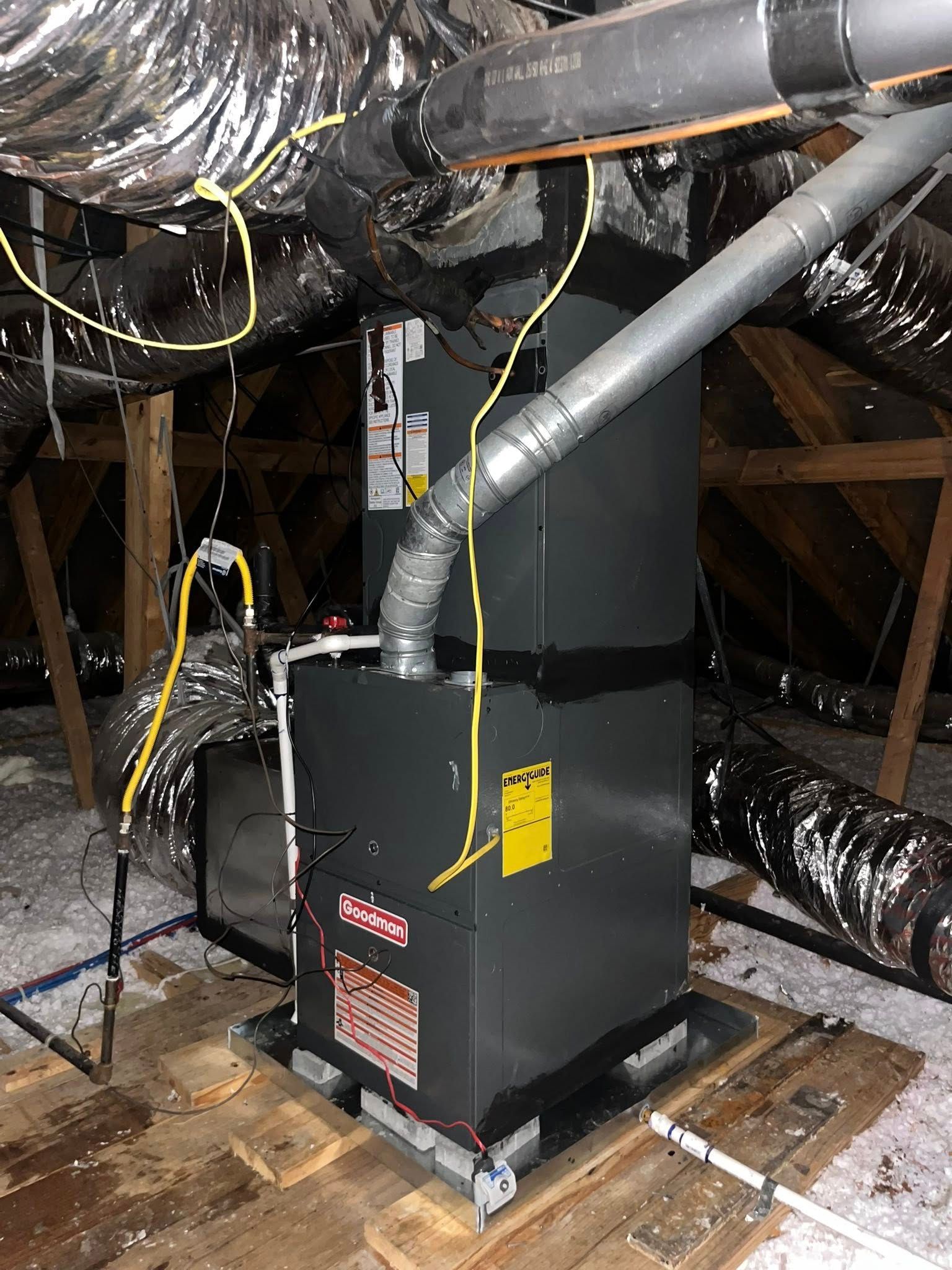 A dark gray furnace in an attic with insulated ductwork and exposed wood beams.