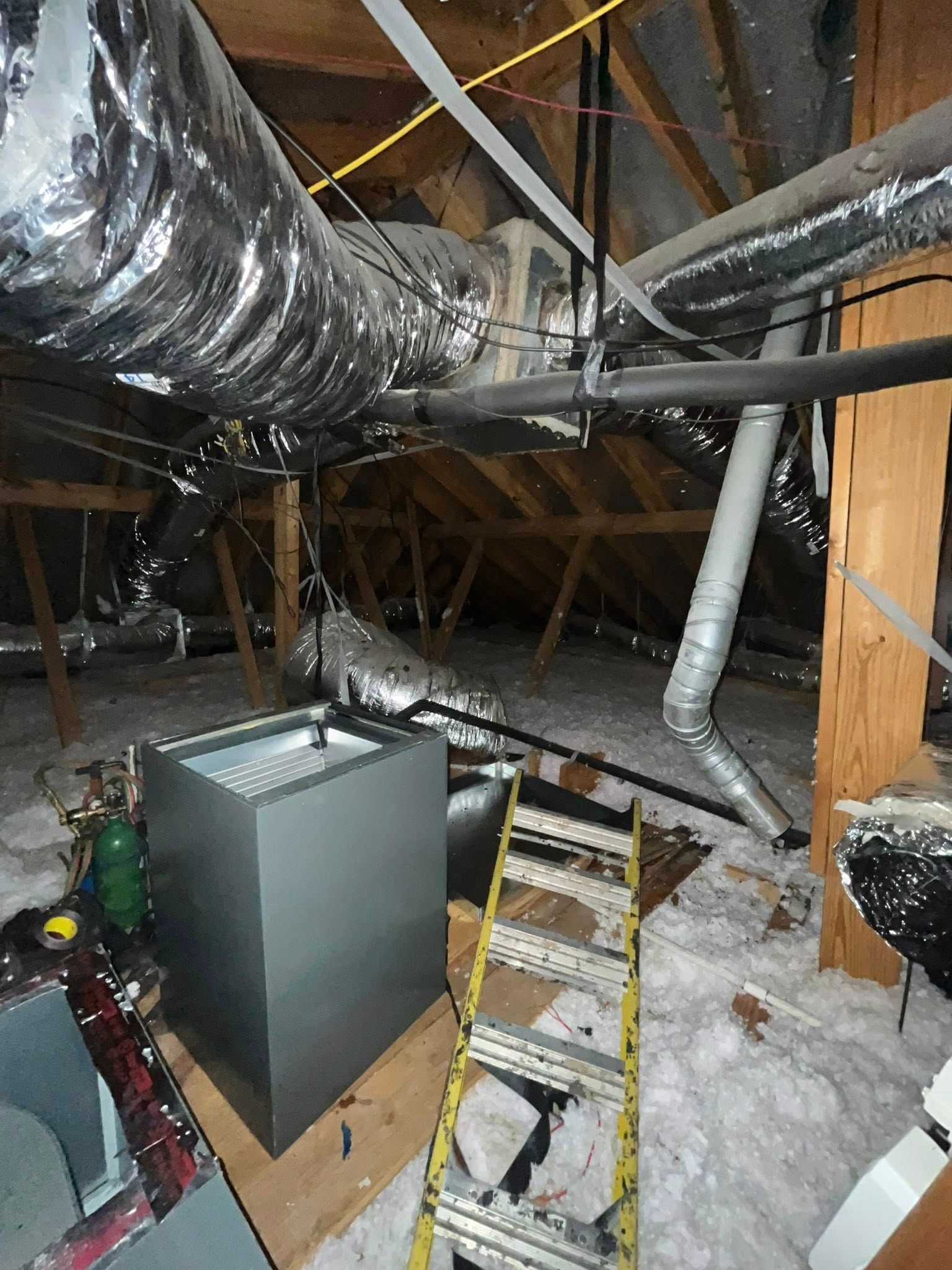 Attic with HVAC system, ductwork, ladder, and insulation. Grey metal furnace.