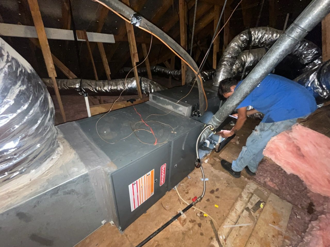 Man working on HVAC unit in an attic with ductwork.