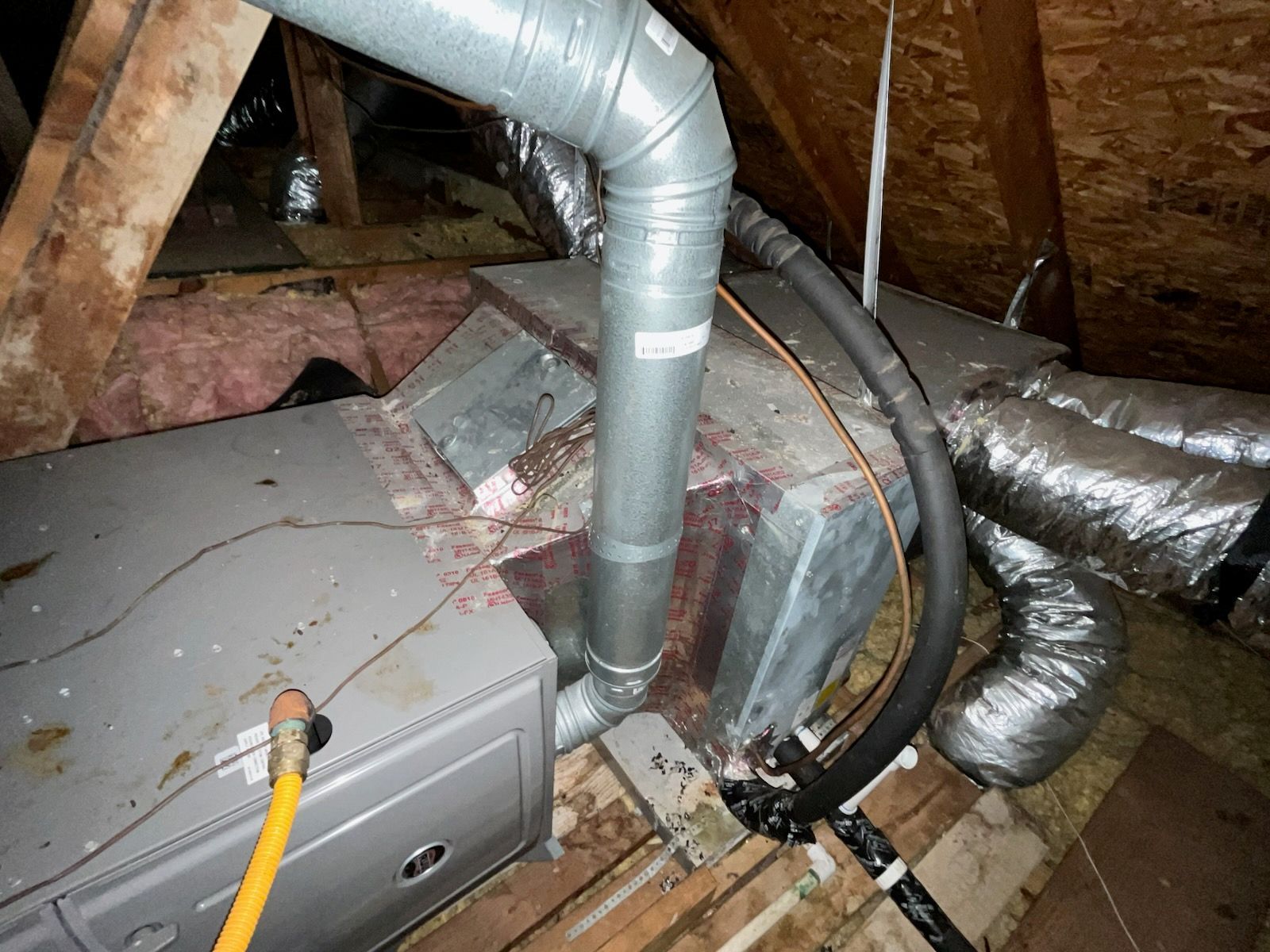 HVAC system in an attic. Gray furnace and ductwork are visible, along with insulation and wooden beams.