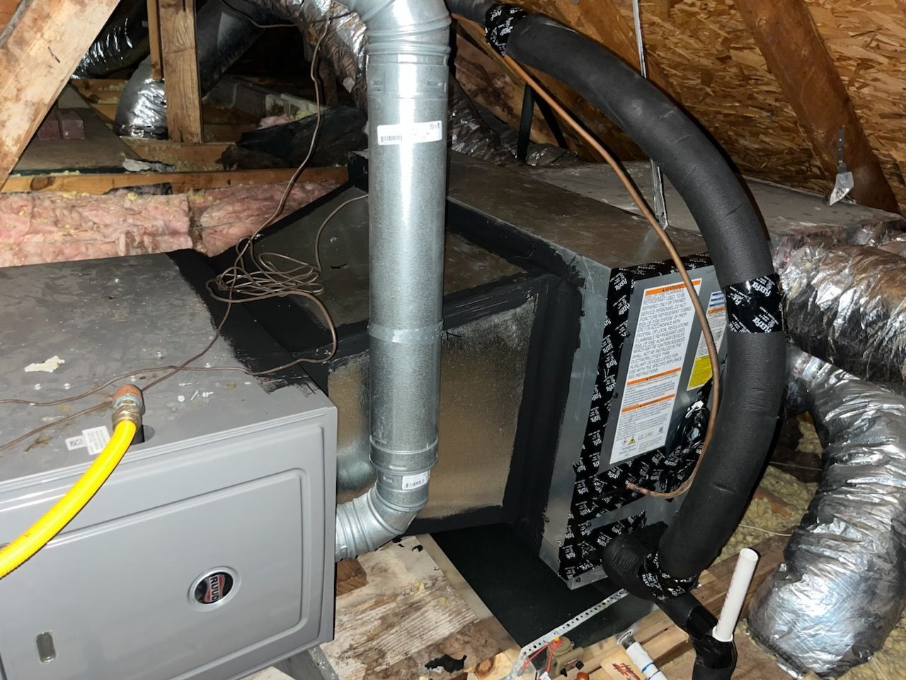 HVAC system in attic: furnace, air handler, insulated ductwork, metal pipes, and yellow gas line.