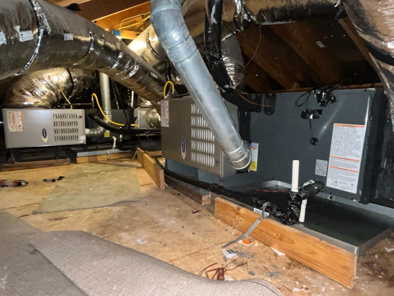 HVAC units in an attic space. Silver ductwork, wooden platform, and insulation are visible.