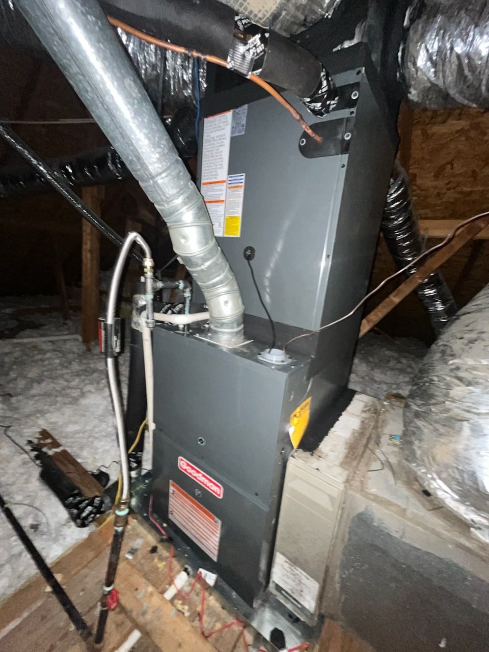 Gray HVAC unit in an attic with ductwork and a vent pipe.
