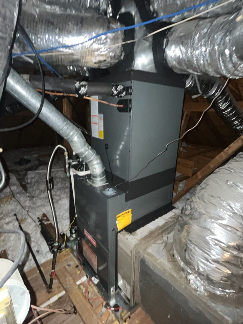 HVAC system in an attic; a gray furnace with ductwork connected; insulated air ducts and support beams.