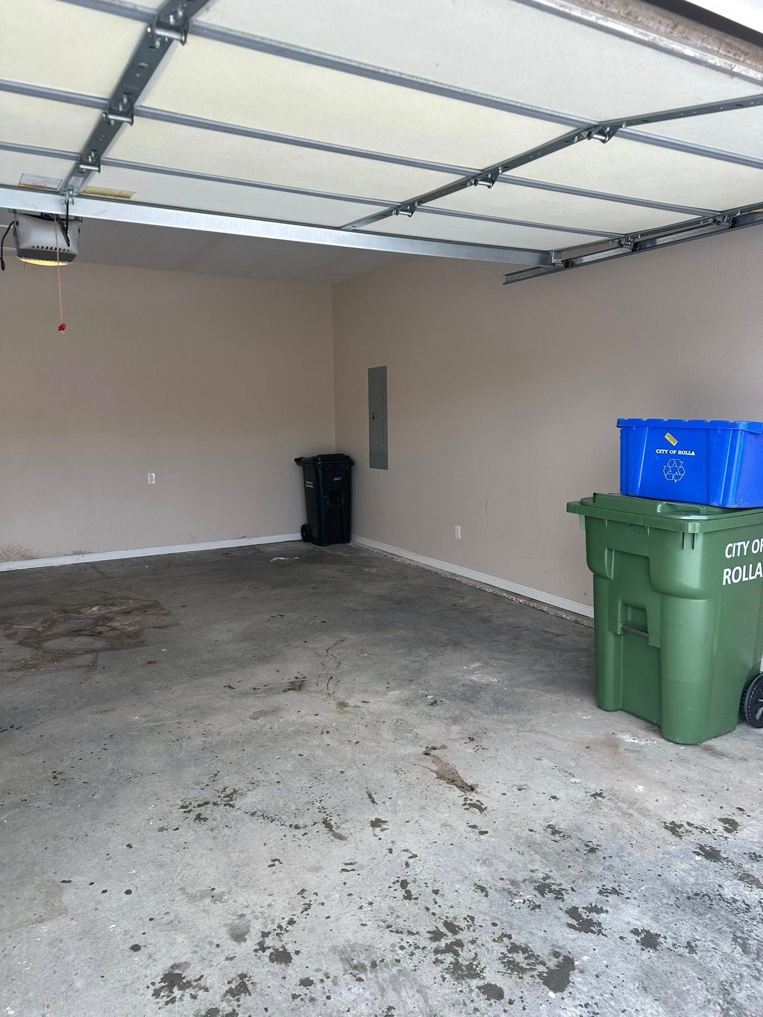 Empty garage with a concrete floor, beige walls, and green and blue trash bins near the right side.
