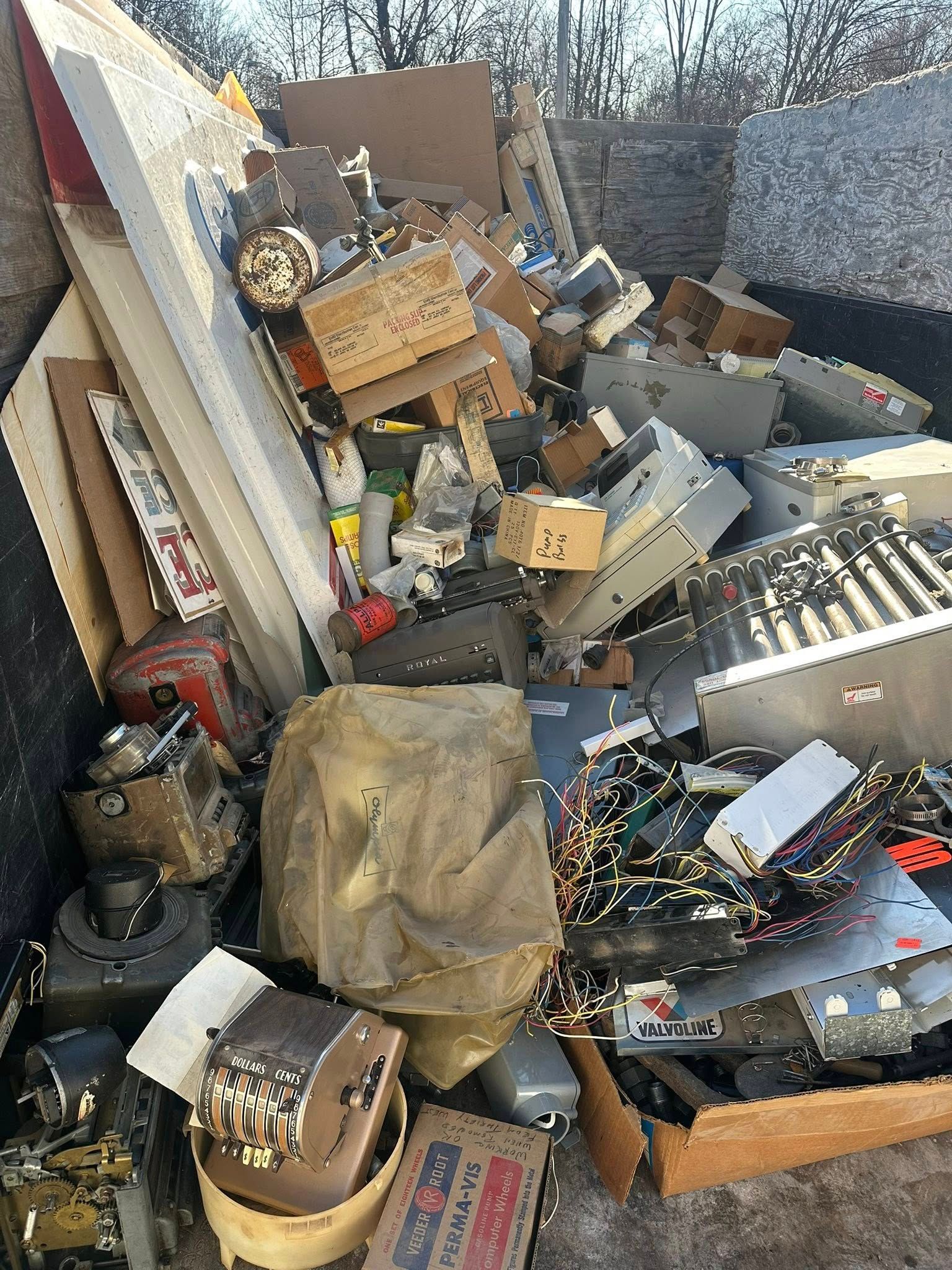 A cluttered pile of scrap metal, boxes, and debris outdoors beside a fence.