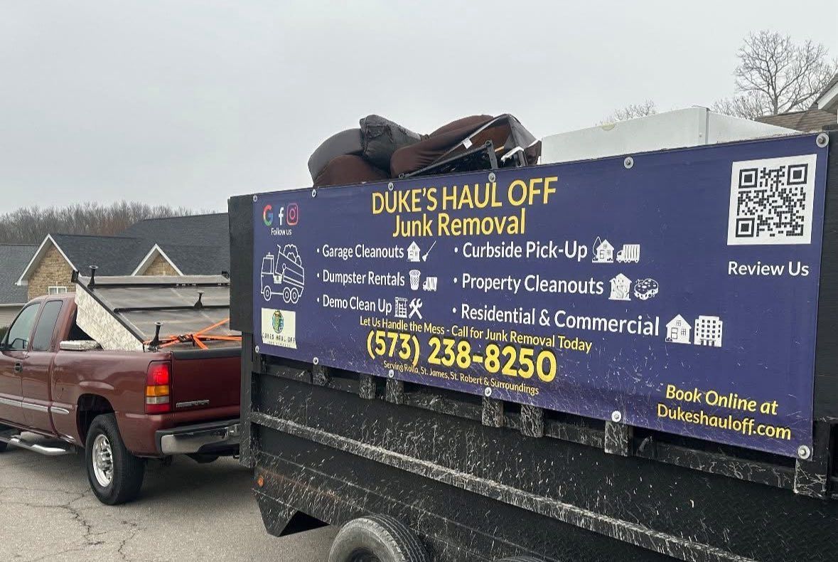 Black junk removal truck with “Mike’s Haul Off” sign, parked beside a red pickup in a snowy lot