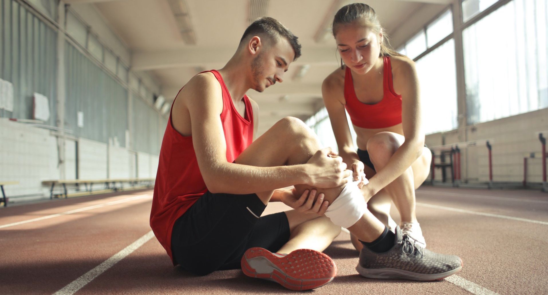 A man and a woman are sitting on the ground on a track . the man is helping the woman with her ankle.