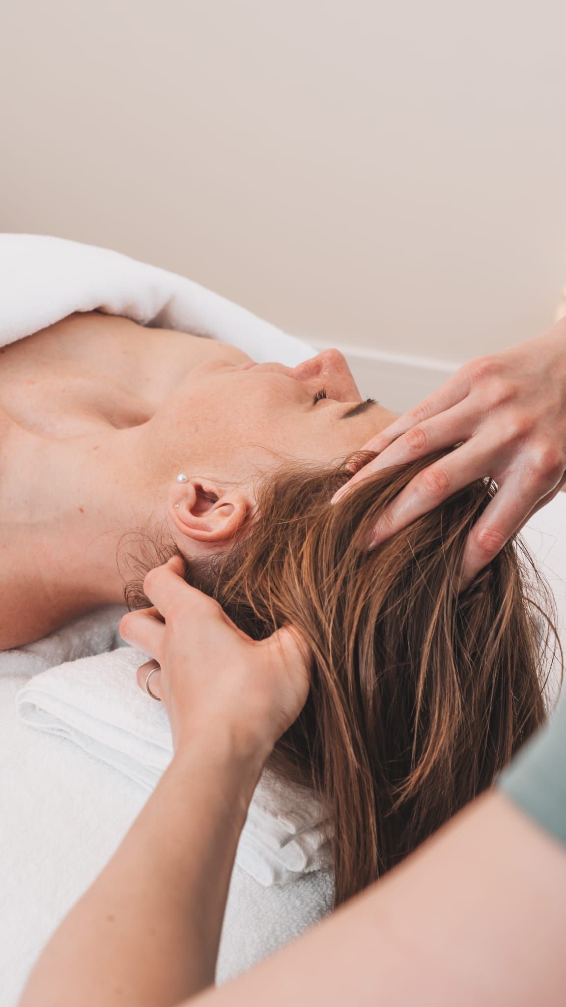 Person receiving head massage, eyes closed, hands on head in spa setting.