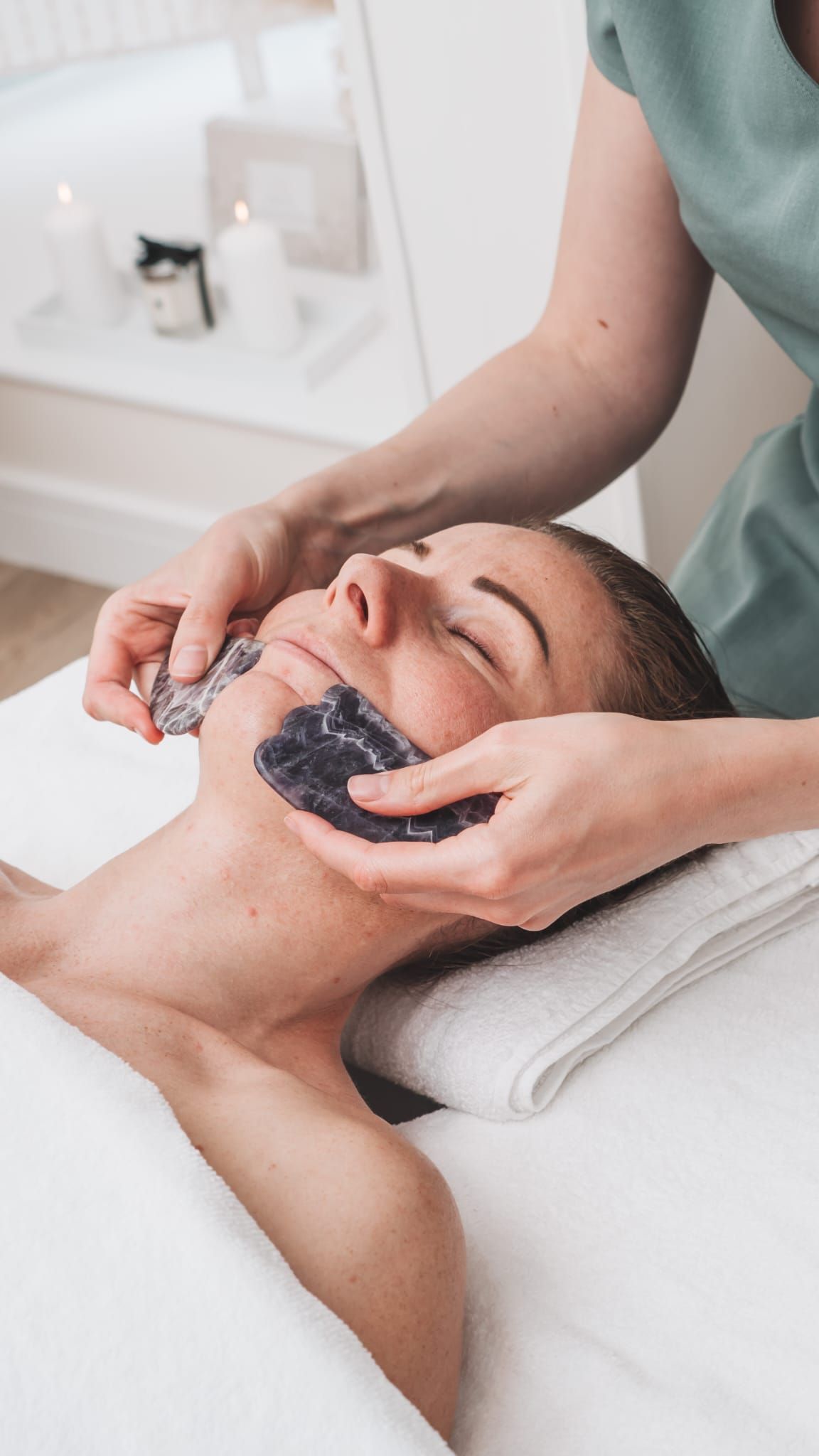 Woman receiving facial waxing at a spa; technician holding wax strips, face relaxed on a towel.