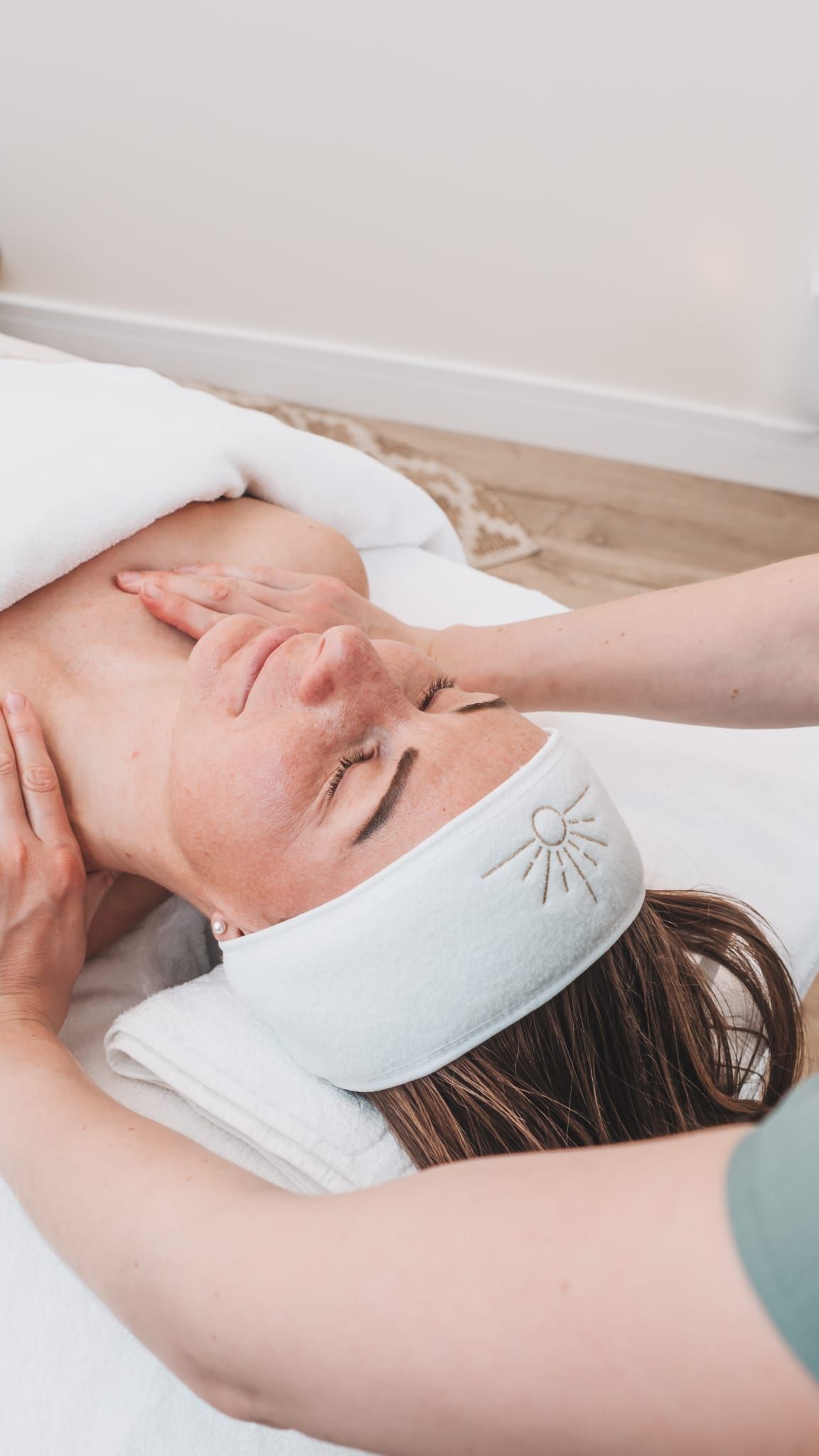 Woman receiving a facial massage at a spa. Hands on face and neck; wearing a headband.