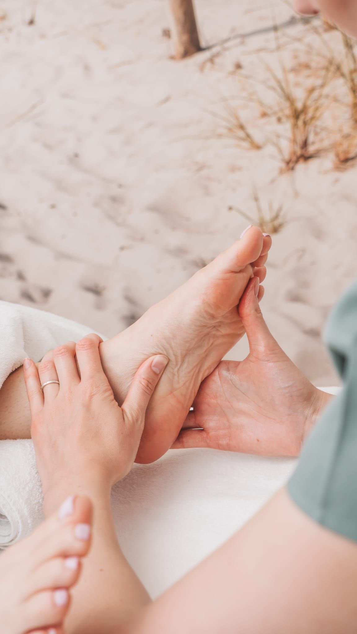 Hands massaging a foot on a towel, beach sand background.