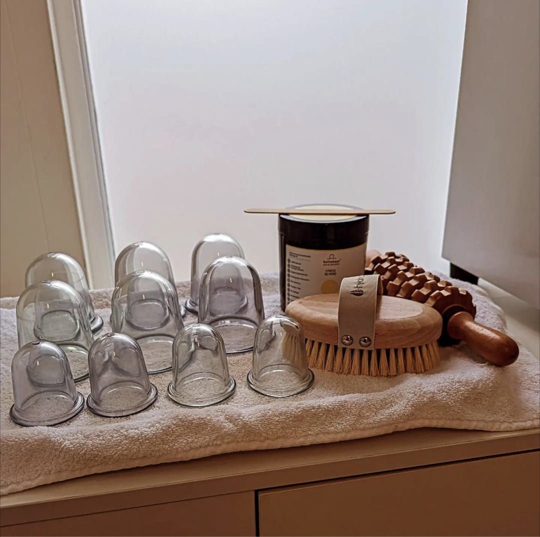 Cupping therapy equipment: glass cups, brush, jar, and roller on a towel.