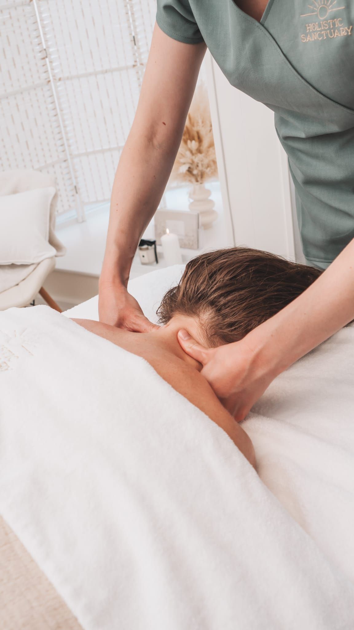 Person receiving neck massage; masseuse in green shirt, white setting.