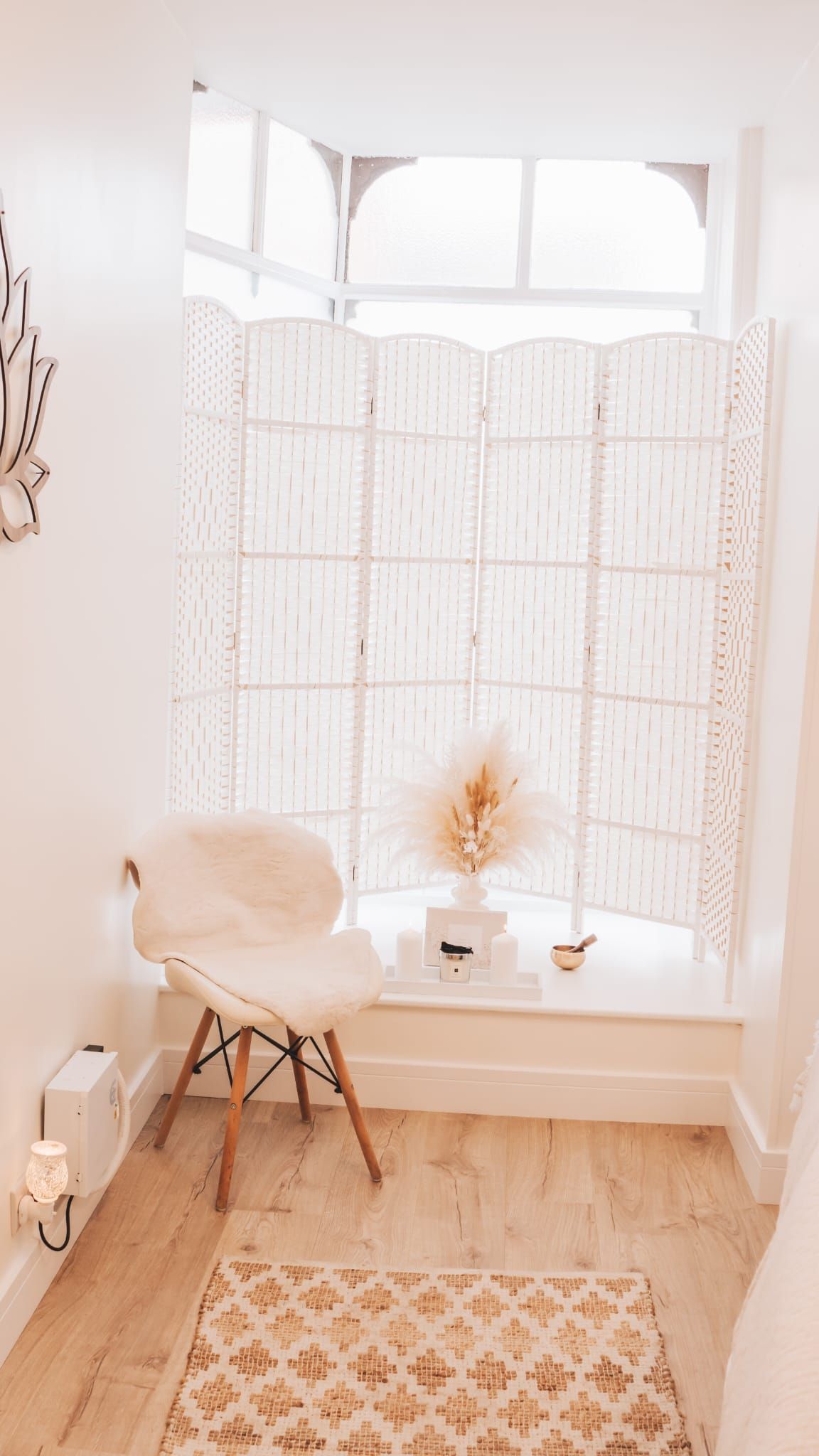 Cozy white-walled alcove with a fluffy chair, patterned rug, and decorative screen in front of a window.
