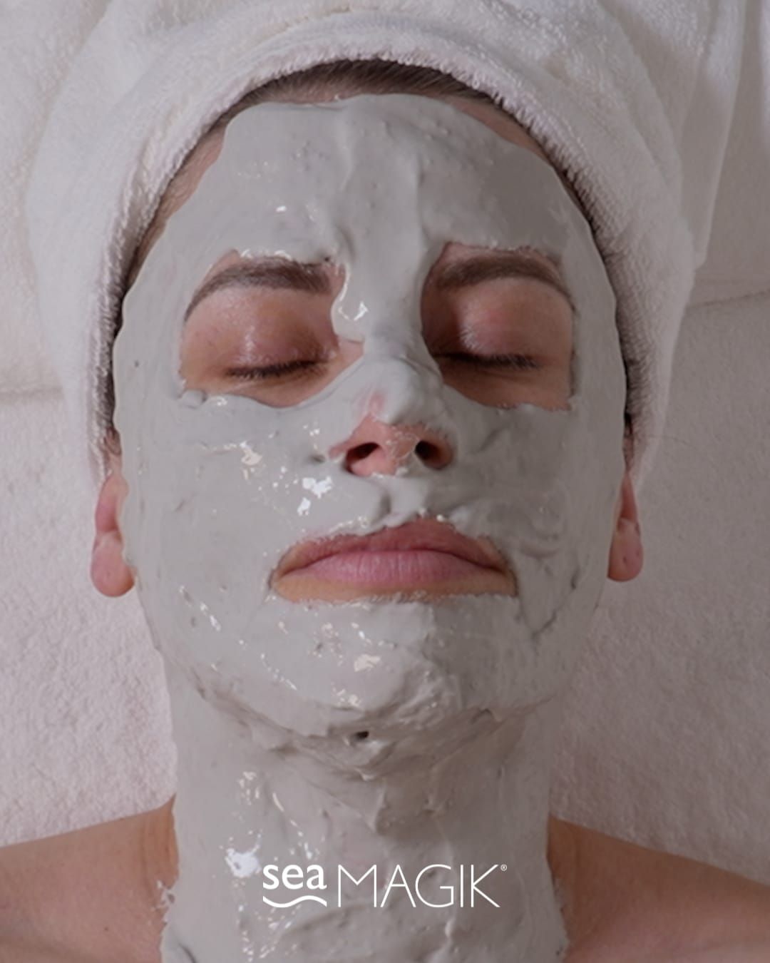 Woman with a grey face mask, eyes closed, resting on a white towel.