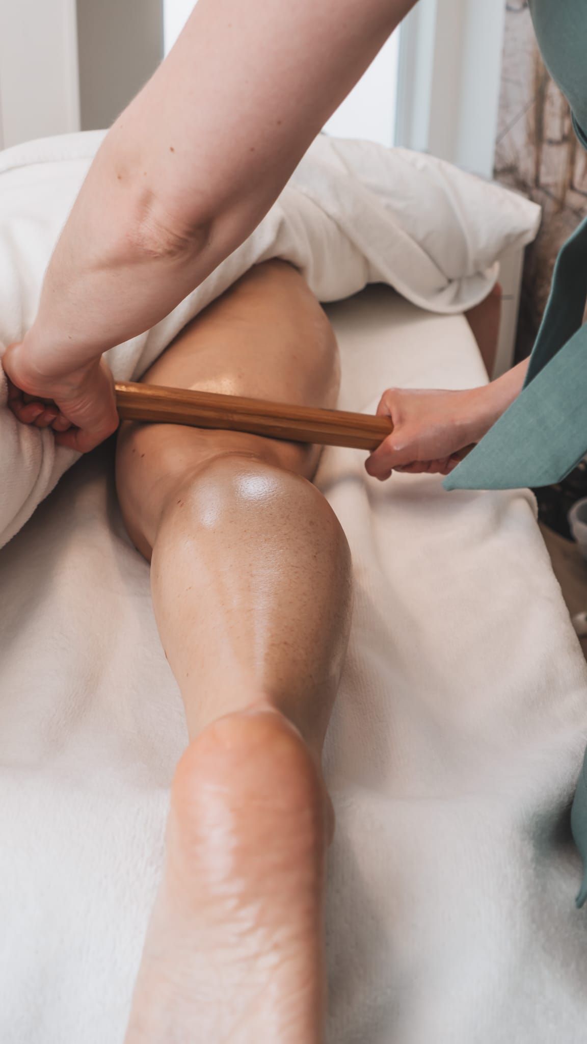 Person receiving a leg massage with a bamboo stick on a massage table.