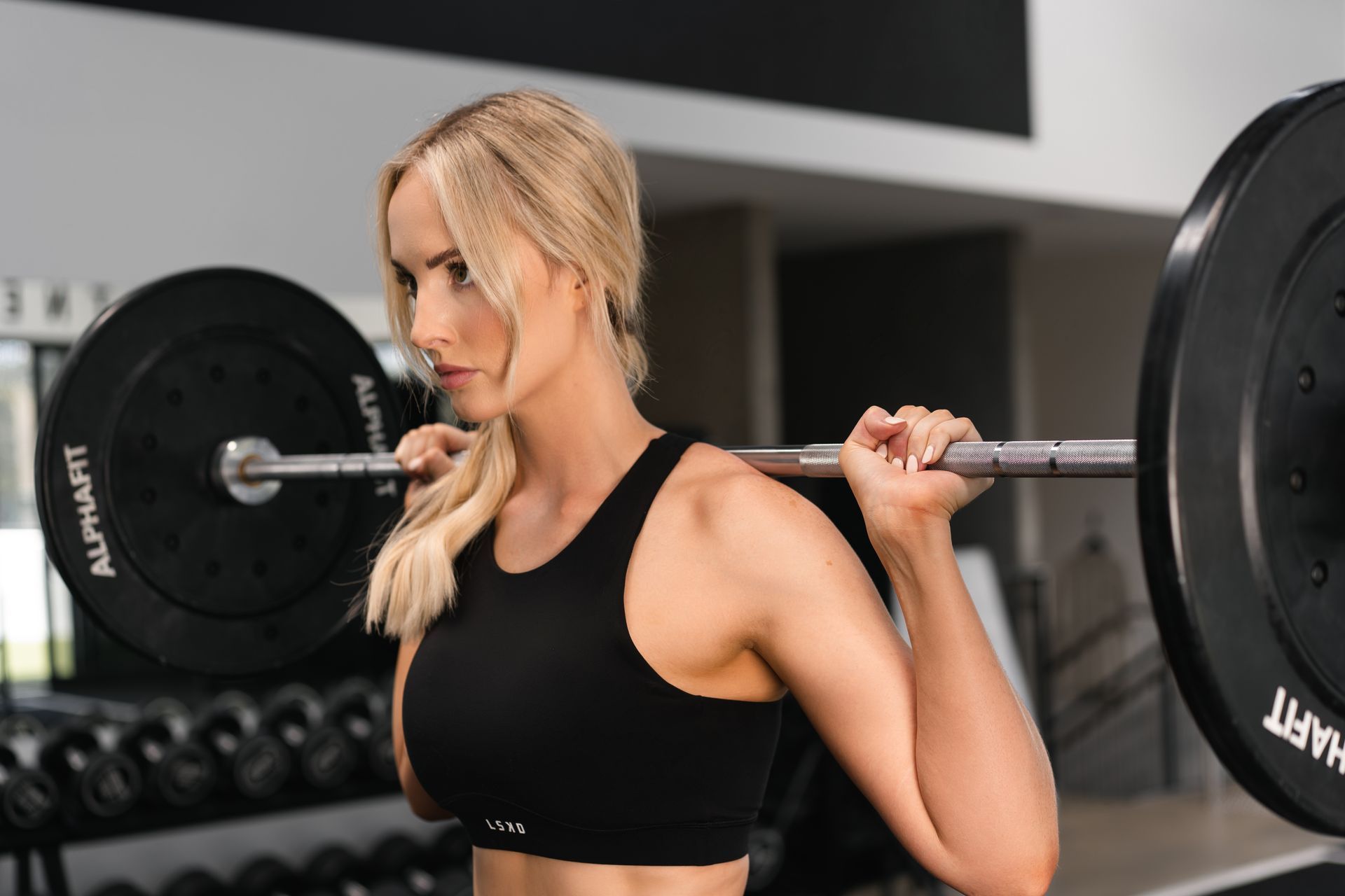 A woman is squatting with a barbell on her shoulders in a gym.