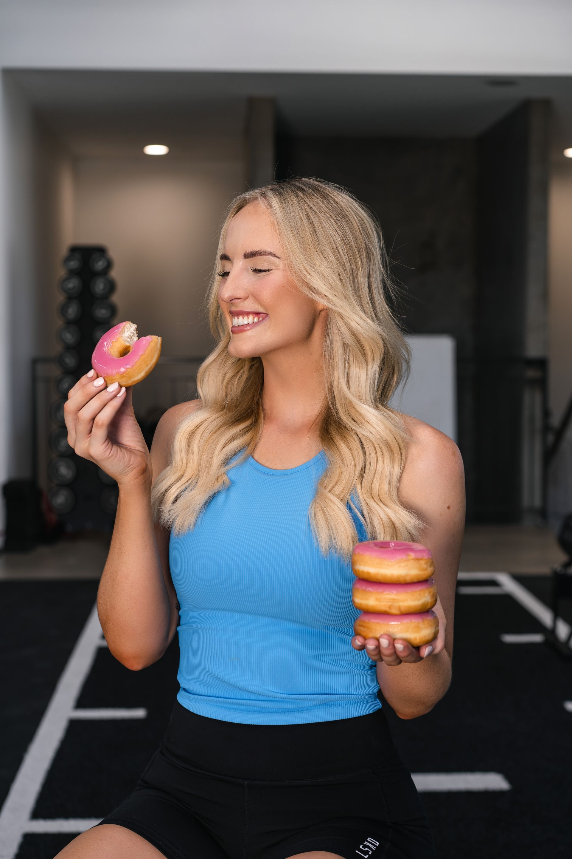 A woman is holding three donuts in her hands and smiling.
