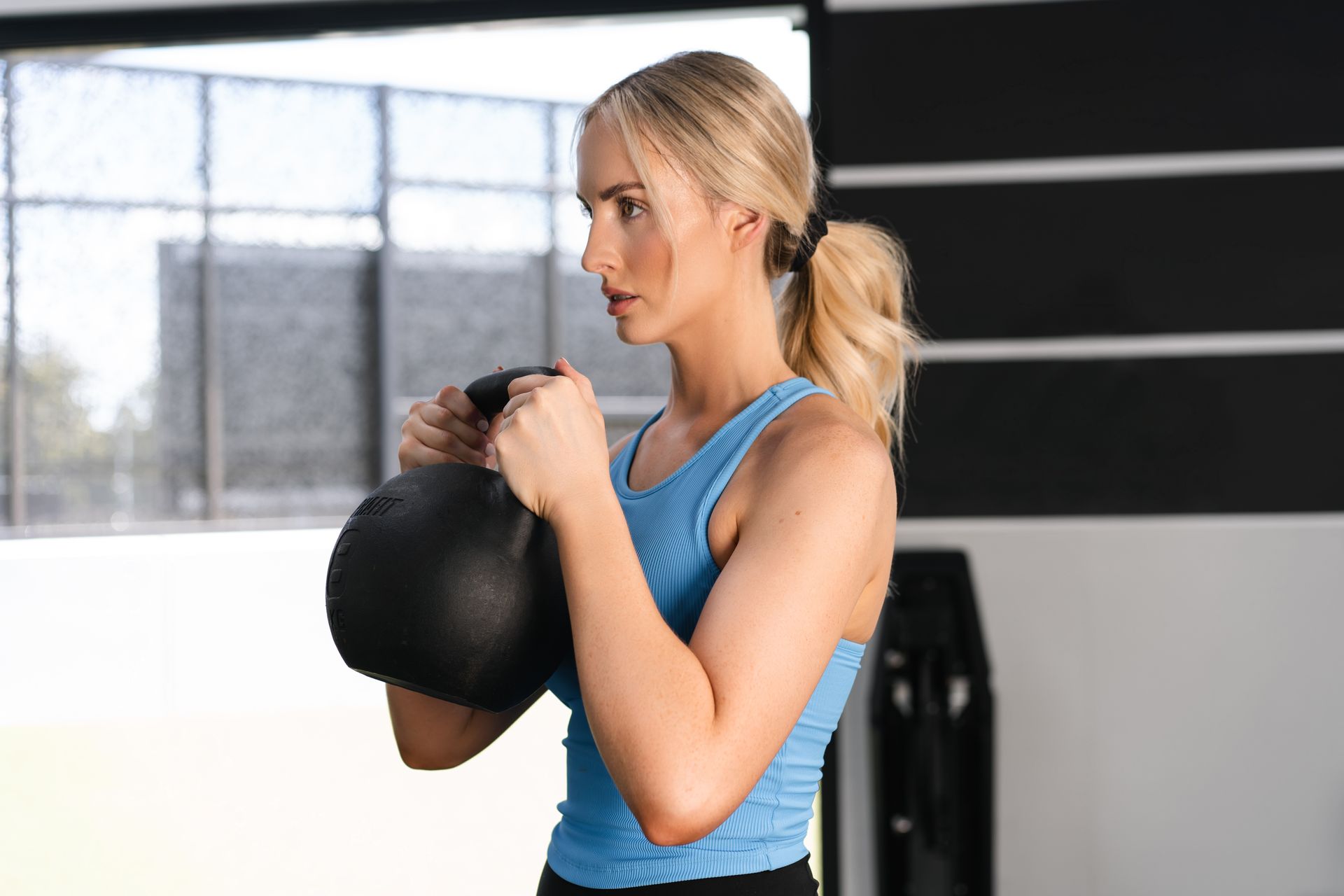 A woman is holding a kettlebell in her hands in a gym.
