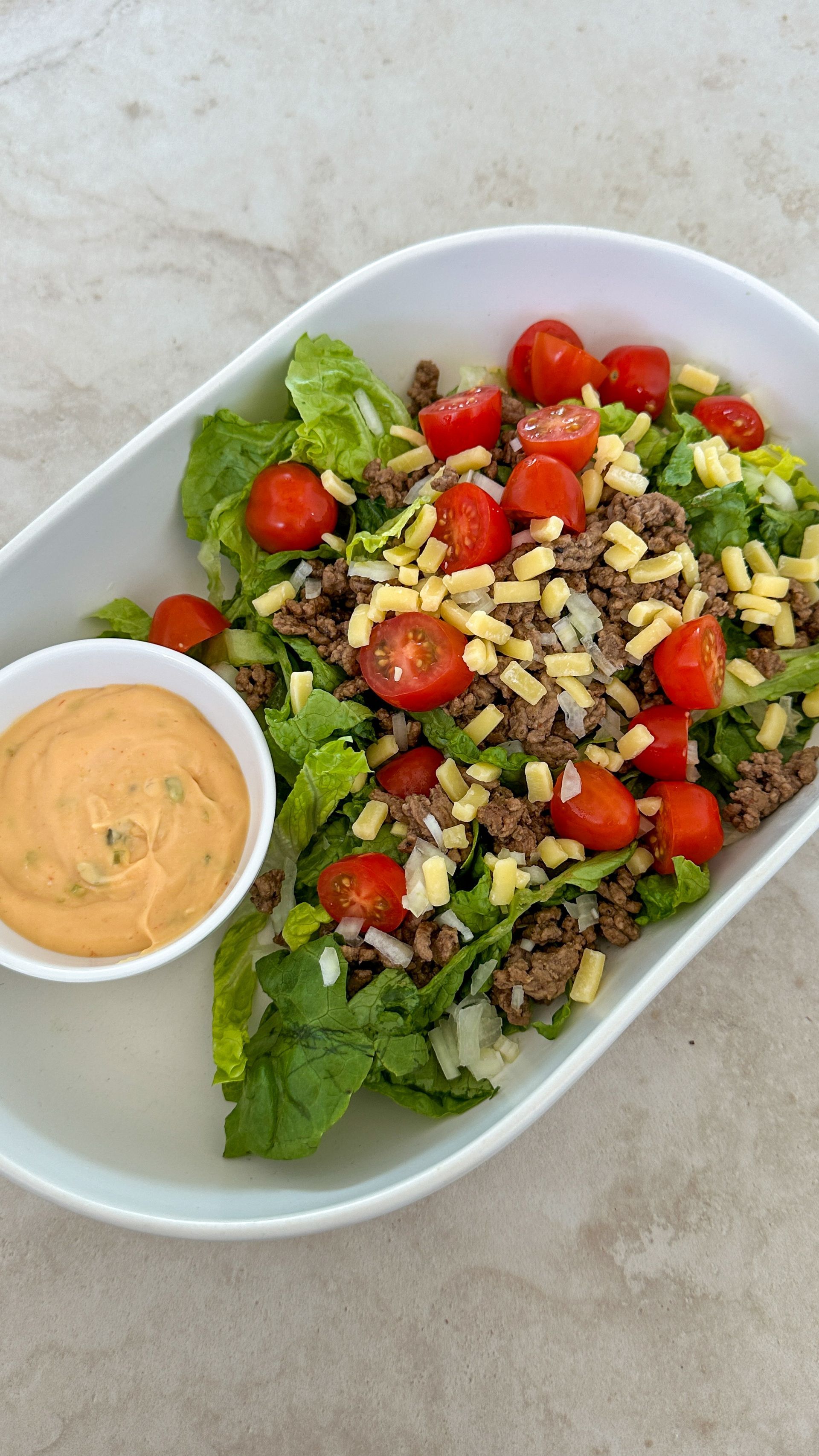 A salad with meat , lettuce , tomatoes and cheese on a plate with a dipping sauce.