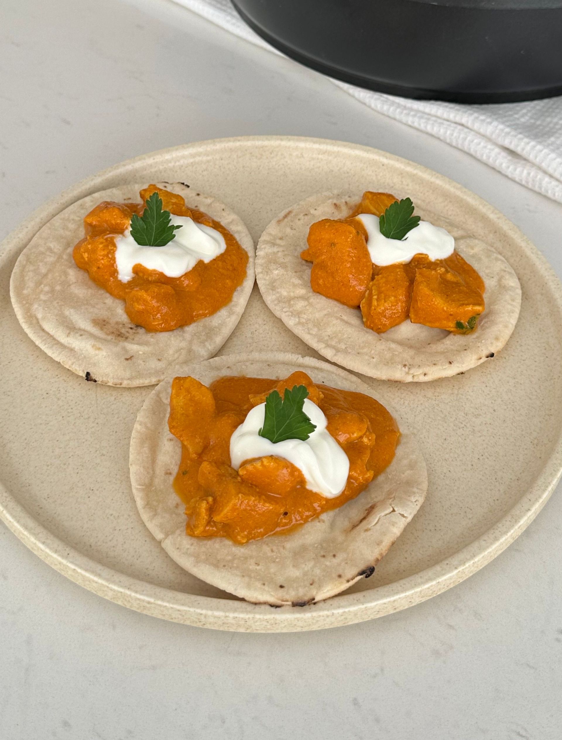 Three tacos with sauce and sour cream on a plate