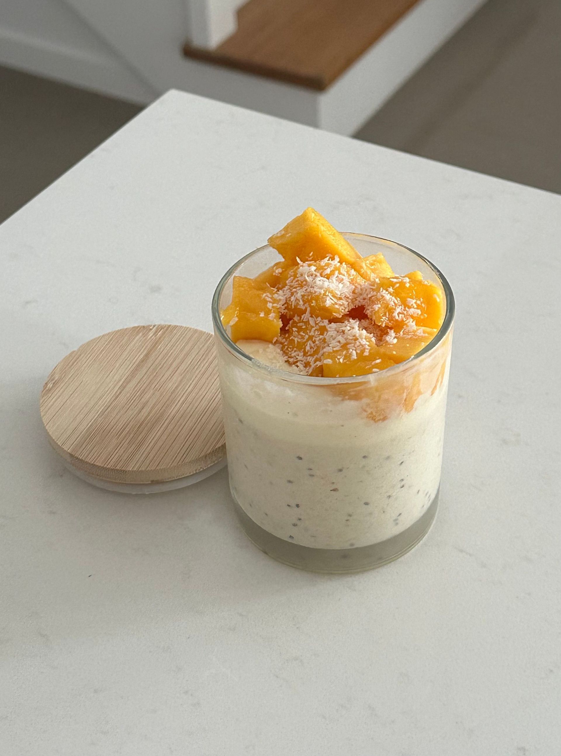 A glass filled with yogurt and mango slices on a table.